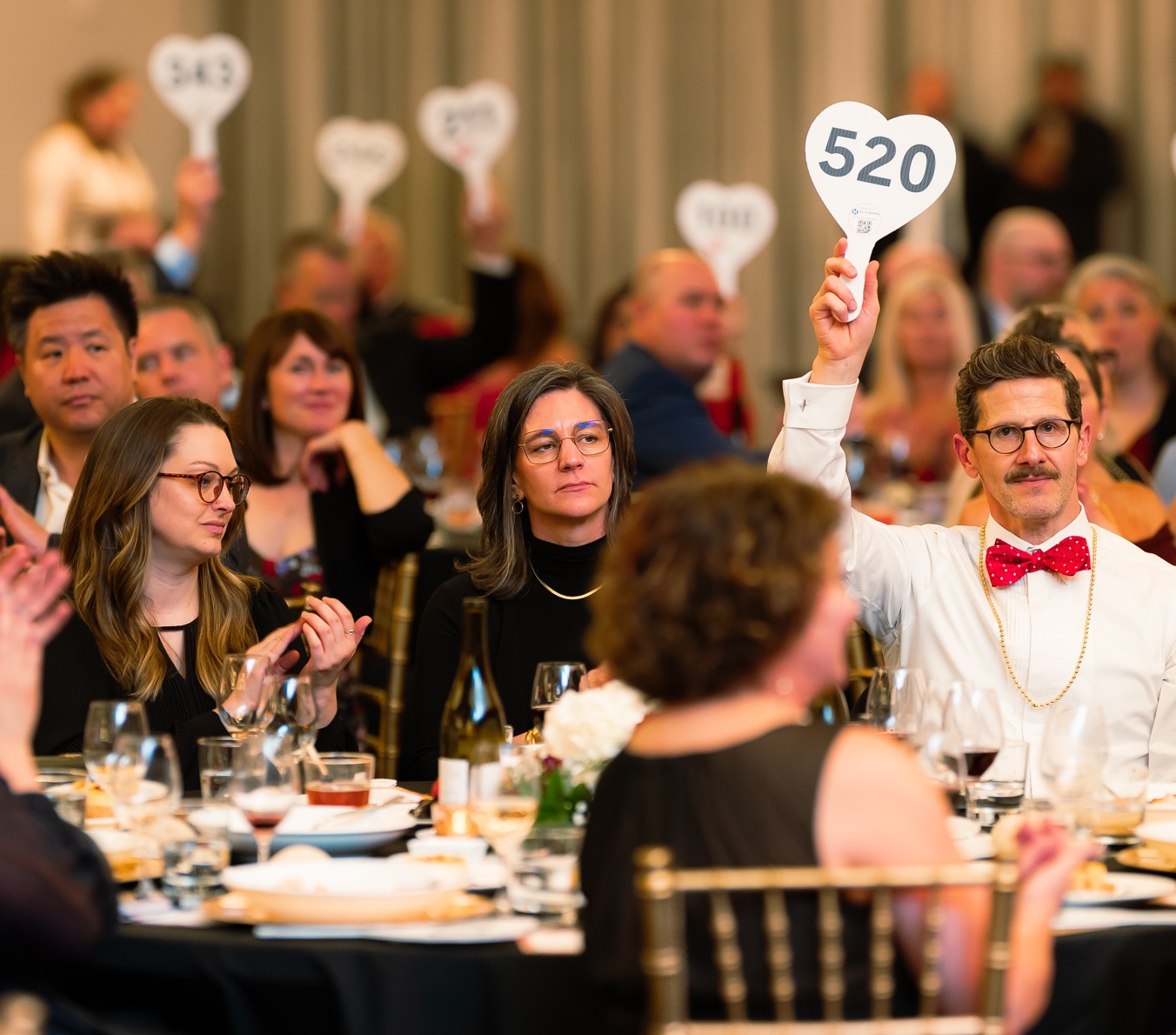 View of room with people holding bidder paddles in the air.